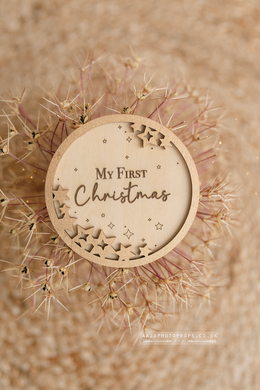 Wooden round plaque with 'My First Christmas' text surrounded by dried flowers on a beige background. 10cm wooden disc. With gold stars and Engraving. My first Christmas photo prop.