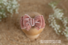 A dusty pink velvet tieback bow on a wooden prop, with white flowers in the background.