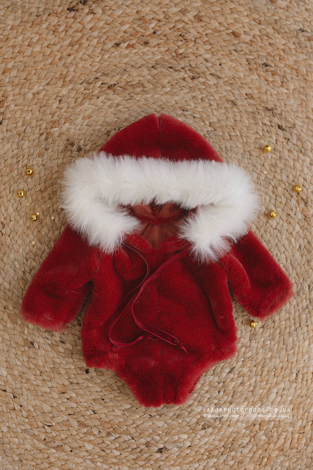 Red baby outfit with white fur trim on a textured brown background