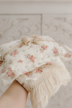 Floral-patterned fabric with fringes held by a hand against a neutral background. newborn posing pillow with velvet bow. boho
