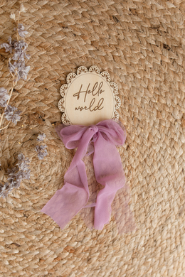 Decorative item with 'Hello world' text on a woven surface with flowers. baby shower, lilac. Engraved