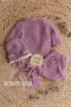 Purple lilac baby outfit with bear bonnet and bloomers on a jute rug with dried larkspur flowers in misty lilac