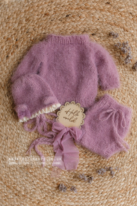 Purple lilac baby outfit with bear bonnet and bloomers on a jute rug with dried larkspur flowers in misty lilac