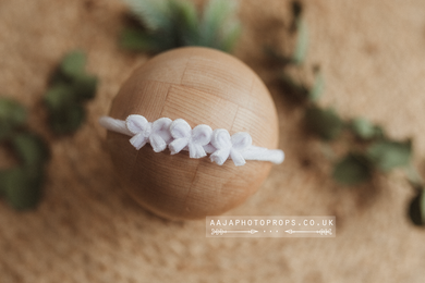 A white velvet hair tie with bows, displayed on a wooden prop.