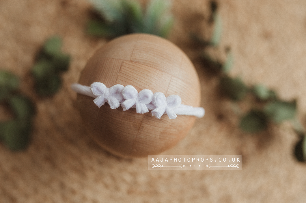 A white velvet hair tie with bows, displayed on a wooden prop.
