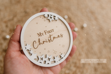 Load image into Gallery viewer, Wooden ornament with &#39;My First Christmas&#39; text held in a hand against a blurred background. Engraved on a disc.