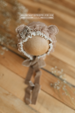 A beige newborn bonnet with bear ears, lace, and velvet ties on a mannequin head.