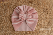 Pink velvet turban hat with bow on a wicker rug.