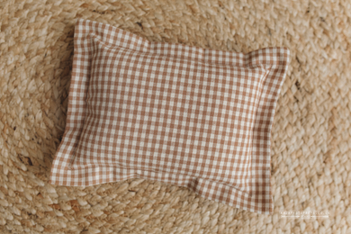Checkered pillow on a textured woven surface. In brown and beige colours. Photo props.