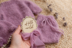 Purple lilac baby outfit with bear bonnet and bloomers on a jute rug with dried larkspur flowers in misty lilac