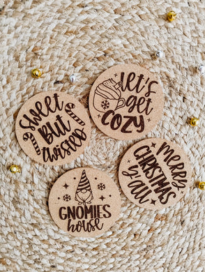 Four cork coasters with Christmas-themed text on a woven surface.