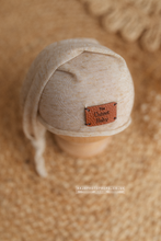 Beige baby bonnet with a label on a textured beige background