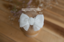 A single off white velvet bow tieback placed on a wooden surface, with a blurred background featuring a floral pattern.